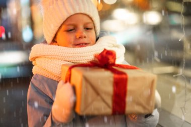 Hediyeler kutusuyla portre çocuk geleneksel Noel pazarında Noel vitrininde alışveriş yapıyor ve hayal kuruyor. Xmas Çocukluk Tatili Konseptini Sunar.