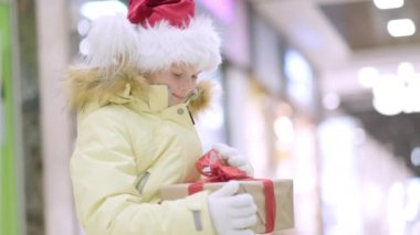 Noel Baba şapkalı küçük kız. Geleneksel alışveriş merkezinde Noel kutusuyla oturuyor. Xmas Çocukluk Tatili Konseptini Sunar.