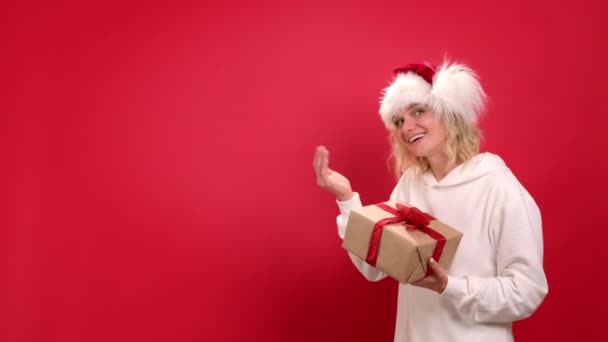 Julhelgen försäljning och shopping Porträtt av glada kvinna i Santa hatt med nuvarande rutan be gå gör kom hit gest inbjudande att komma på röd studio bakgrund. Hallå där, kom hit. — Stockvideo