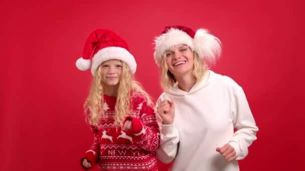 Рождественские каникулы Портрет счастливая семья из двух В Санта-Шапки мать и дочь танцуют и улыбаются на красном фоне студии — стоковое видео