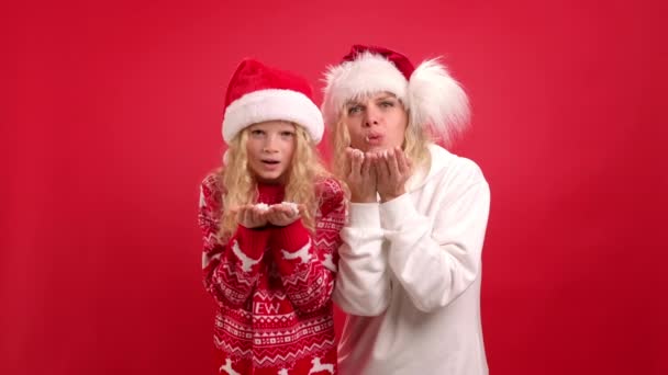 Jul semester Porträtt lycklig familj av två I Santa hattar mor och dotter har kul att kasta snö och blåsa snö av sina händer på röd studio bakgrund — Stockvideo