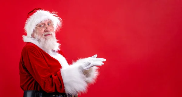 Święty Mikołaj odsuwając na bok pustą przestrzeń na palcu i pokazując puste miejsce dla reklamowanego produktu lub tekstu na czerwonym tle studio. Wyprzedaż, rabat, Czarny Piątek. Spójrz na to.. — Zdjęcie stockowe