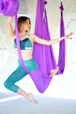 Genç, gülümseyen kadın salıncakta sallanıyor. Havadan uçan yoga egzersizleri spor salonunda mor hamakta pratik yapıyor.