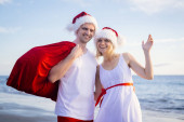Šťastná rodina v Santa Claus klobouky slaví Vánoce na pláži. Usmívající se lidé cestují do teplých zemí na zimní turné. Nový rok a vánoční turisté.
