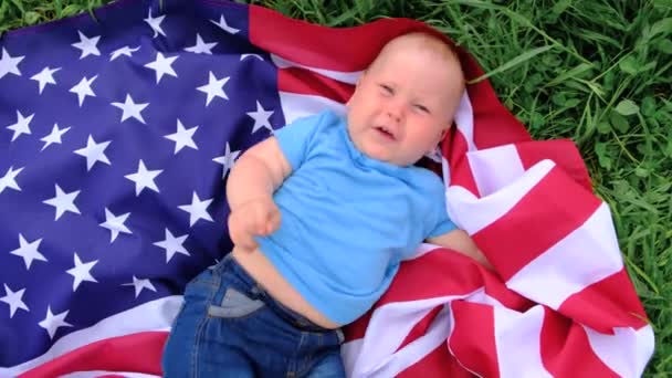 Ενθουσιασμένο μωρό που βρίσκεται σε εθνική σημαία των ΗΠΑ σε εξωτερικούς χώρους πάνω από το καλοκαίρι πράσινο γρασίδι - αμερικανική σημαία, χώρα, πατριωτισμός, ημέρα μνήμης ανεξαρτησίας 4η Ιουλίου — Αρχείο Βίντεο