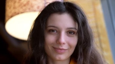 Çekici, gülümseyen Avrupalı esmer kızın portresi. Kafede oturan kadın kameraya bakıyor ve gülümsüyor.