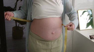 Hamile karnını santimetre bant ile ölçen genç bir kadın. Doğum hazırlığı, büyük göbekli kız sağlıklı hamilelik.