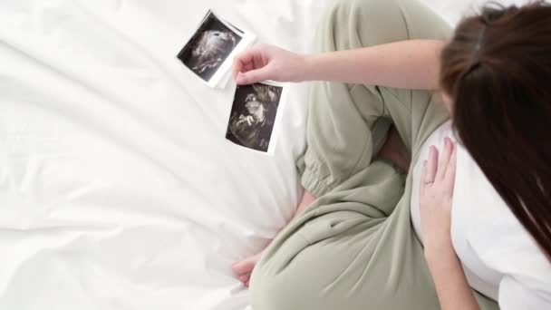 Вид сверху: беременная женщина смотрит ультразвуковое фото плода, стоящего дома, молодая будущая мама, ожидающая первого ребенка, концепция беременности и материнства. — стоковое видео