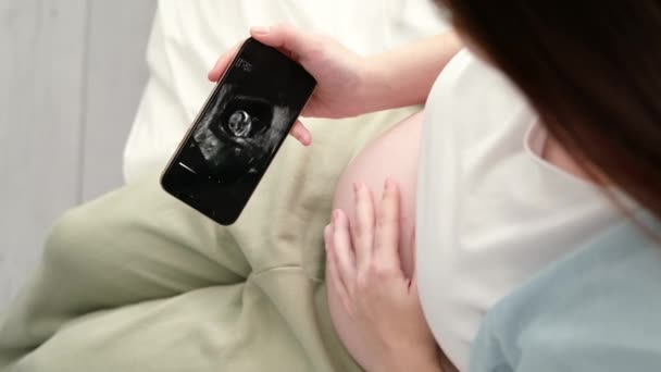 Vista superior recortado de la mujer embarazada buscando ultrasonido de vídeo en el teléfono del feto de pie en casa, joven futura mamá esperando niño primer bebé, el embarazo y el concepto de maternidad 7.1.22 StPetersburg Rusia. — Vídeos de Stock