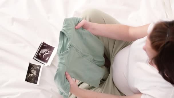 Top view Έγκυος μητέρα κρατώντας τα ρούχα του μωρού στα χέρια, Happy Προσδοκώμενη μητέρα περιμένει παιδί. Προετοιμασία για τον τοκετό, Κορίτσι μεγάλη κοιλιά προχωρημένη εγκυμοσύνη, την έννοια της μητρότητας. — Αρχείο Βίντεο