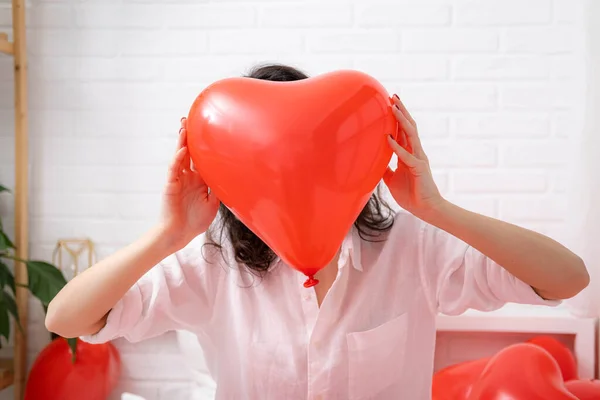 Шарик в форме красного сердца закрывается в руках брюнетки улыбающейся девушки на День Святого Валентина. — стоковое фото