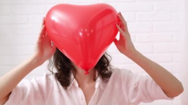 Kırmızı kalp şeklinde balon Sevgililer Günü 'nde gülümseyen esmer kızın ellerinde.. 