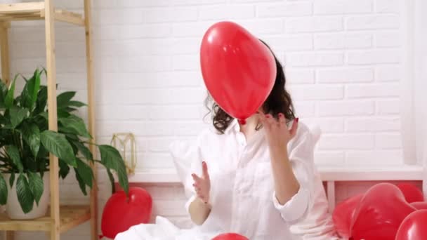 Brunetka Europejska dziewczyna cieszy się bawiąc się na łóżku z czerwonym kształcie serca balony. Poranna miłość niespodzianka prezent na Walentynki — Wideo stockowe