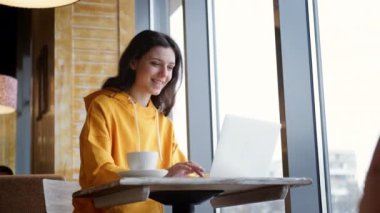 Çevrimiçi eğitim ve iş öğrenme mesafesinde Kafe 'de çalışan mutlu kadın bilgisayarla çalışıyor ve kahve içiyor.