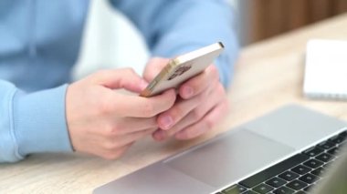  Adam iPhone 12 'yi kullanıyor. Parmak basıyor, sosyal medya daktilo metni okuyor ya da internetten alışveriş yapıyor. Cep telefonu iki elinle evde ya da işte. Masa 24.04.21 St. Petersburg Rusya 'daki bilgisayar.