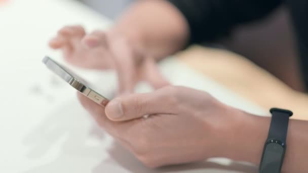 Άνθρωπος που χρησιμοποιεί το iPhone 12 smartphone πατώντας το δάχτυλο, διαβάζοντας τα μέσα κοινωνικής δικτύωσης πληκτρολογώντας κείμενο ή αγορές σε απευθείας σύνδεση. Κινητό τηλέφωνο σε δύο χέρια στο σπίτι ή στη δουλειά. laptop στο τραπέζι 24.04.21 Αγία Πετρούπολη Ρωσία — Αρχείο Βίντεο