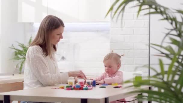Μαμά και μικρή κόρη κάθονται στην κουζίνα και παίζουν πολύχρωμη πλαστελίνη Μητέρα και κόρη γελάνε διασκεδάζοντας μαζί — Αρχείο Βίντεο