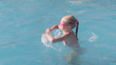 Yüzme havuzunda yüzen küçük bir kız, eğlenen bir çocuk, su sıçratan, atlayan bir çocuk. Yaz tatili aile tatili turistleri.