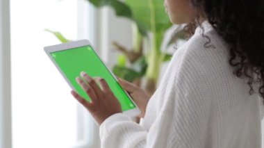iPad tableti kullanan Afro-Amerikalı siyahi kız yeşil ekran baskısına göz atıyor kroma tuşuna çevrimiçi yazı okuyor sosyal medya Freelancer Uzaktan çalışıyor evde.