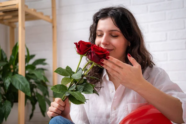 Lány szerelmes csokor rózsa virágok az ágyon piros szív alakú lufik. A nő örül az ajándéknak Valentin-napon. Könnyű lány hosszú hajjal pozitív érzelmeket fejez ki Valentin-napon Jogdíjmentes Stock Képek