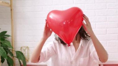 Kırmızı kalp şeklinde balon Sevgililer Günü 'nde gülümseyen esmer kızın ellerinde.. 