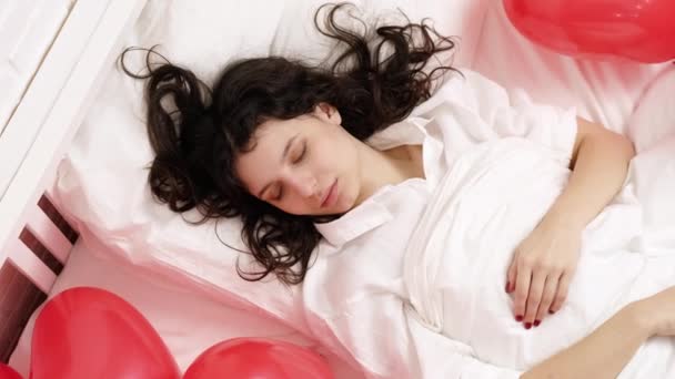 Bruneta evropská dívka spí na posteli s červeným srdcem ve tvaru balonků. Ranní překvapení dárek na Valentýna — Stock video