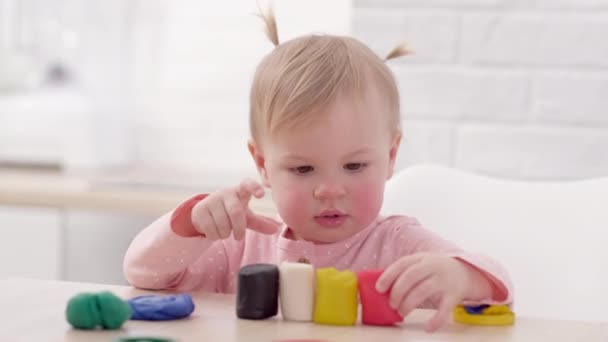 Милая маленькая девочка с забавными хвостиками на голове, сидя на кухне и играя в разноцветный пластилин, 2 года Малышка весело с моделированием глины дома, раннее образование и развитие. — стоковое видео