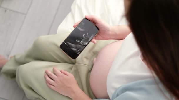 Pandangan utama tentang wanita hamil yang melihat video USG di telepon janin yang berdiri di rumah, ibu masa depan yang masih muda menunggu bayi pertama, kehamilan dan konsep keibuan 7.1.22 StPetersburg Rusia. — Stok Video