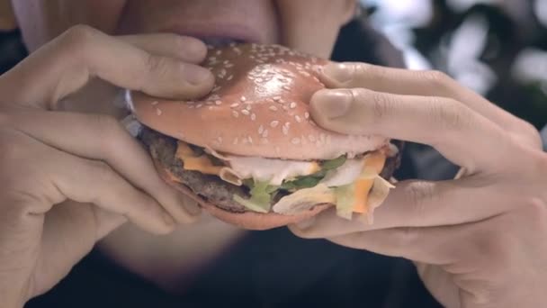 Boca close-up Homem estudante come hambúrguer no restaurante fast food Suculento delicioso hambúrguer grande com carne, queijo de salada e tomate dentro. Nutrição não saudável, lanches, junk food. — Vídeo de Stock