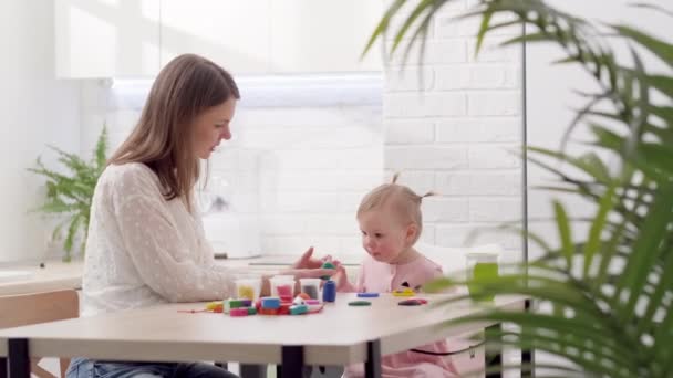 Μαμά και μικρή κόρη κάθονται στην κουζίνα και παίζουν πολύχρωμη πλαστελίνη Μητέρα και κόρη γελάνε διασκεδάζοντας μαζί — Αρχείο Βίντεο