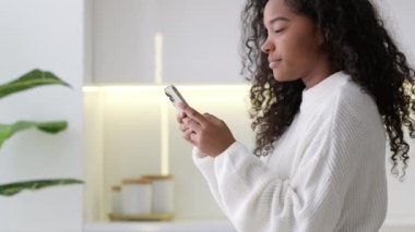 Afro-Amerikalı Kız evde akıllı telefon kullanıyor, parmak basıyor, sosyal medya interneti okuyor, mesaj yazıyor ya da online cep telefonunu iki siyah elle alıyor..
