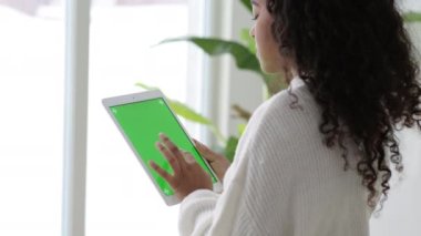 iPad tableti kullanan Afro-Amerikalı siyahi kız yeşil ekran baskısına göz atıyor kroma tuşuna çevrimiçi yazı okuyor sosyal medya Freelancer Uzaktan çalışıyor evde.