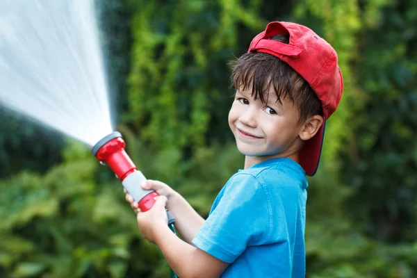 Menino em gorro derrama água ao ar livre — Fotografia de Stock