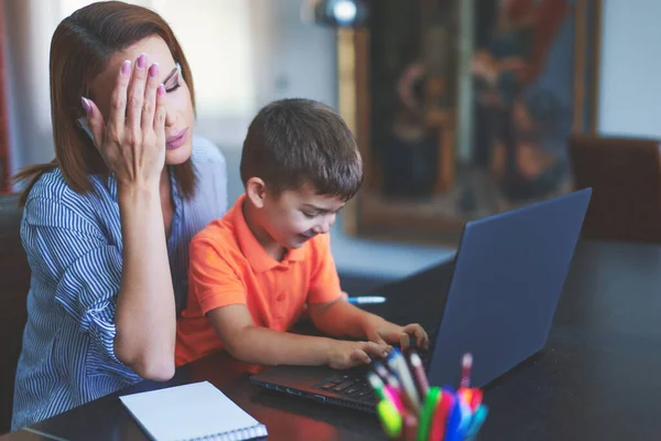 Trött Ung Mor Hemmakontoret Håller Huvudet Medan Son Skriva Bärbar — Stockfoto