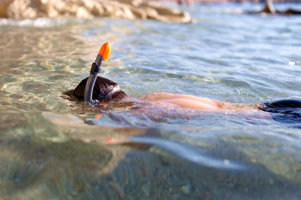 Boy in goggles and pipe diving in sea at rocky shore