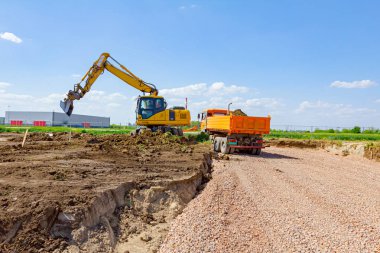 Tekerlekli kazıcı toprağı kazıyor ve çöp kamyonunu inşaat alanında toprakla dolduruyor..