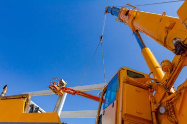 Crane 'in hidrolik pistonu sanayi binasının dev beton iskeletini birleştiriyor. İnsanlar devasa inşaatın beton kirişinin yapımına yardım ediyor..