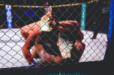 İki güçlü kaslı profesyonel MMA dövüşçüsü, birbirlerine kenetlenmişler, sekizgen katta parterre güreşiyorlar..