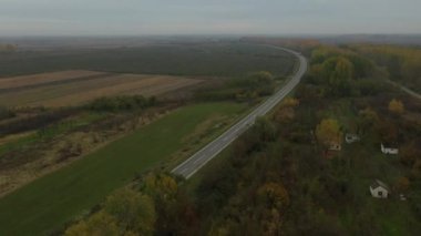 En tepede hareket eden doli üzerinde, ufukta belirsizlik, manzara bitki örtüsü, orman arasında uzanan asfalt yol, kır evi ağaçlı tarım arazileri, aktif trafik. 