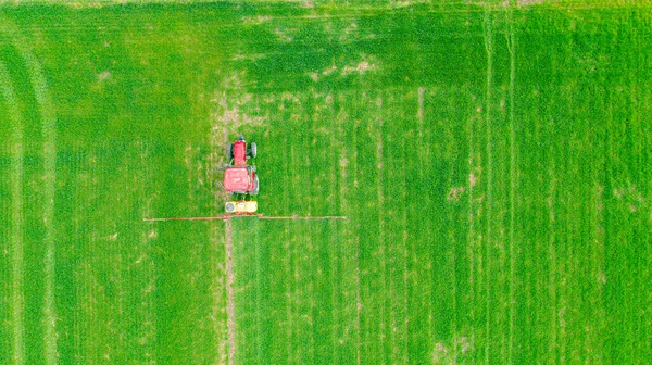 Above top view, overhead view on tractor as spraying farmland with young green wheat dragging mounted wide agricultural sprayer over field.