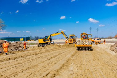 Dikenli ve buldozerli yol silindiri, inşaat alanındaki yol temeli için kum seviyesini düşürüyor..