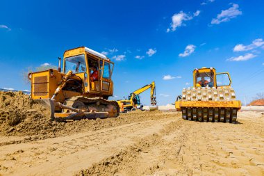 Dikenli ve buldozerli yol silindiri, inşaat alanındaki yol temeli için kum seviyesini düşürüyor..