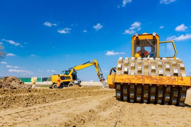 Buldozer ve kazıcılarda çiviler olan patenler inşaat sahasında yol temeli için kumu düzleştiriyor..