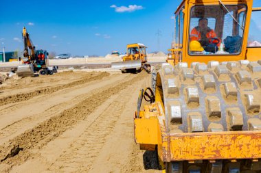 Dikenli ve buldozerli yol silindiri, inşaat alanındaki yol temeli için kum seviyesini düşürüyor..
