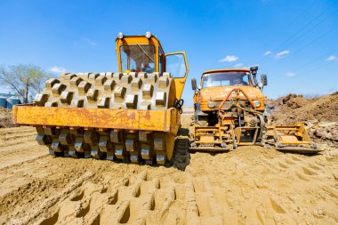 Çivili yol silindiri ve plaka titreşim sıkıştırıcılı kamyon inşaat alanındaki yol temeli için kumu düzleştiriyor..