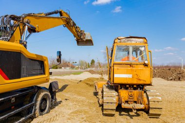 İnşaat alanındaki yol temeli için kum seviyesini ayarlayan buldozer ve kazıcıya arkadan bak, mekanizasyon.