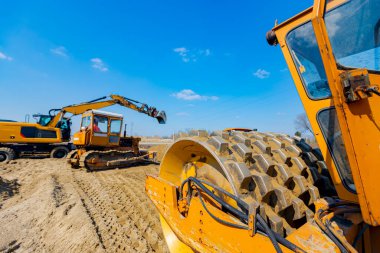 Buldozer ve kazıcılarda çiviler olan patenler inşaat sahasında yol temeli için kumu düzleştiriyor..