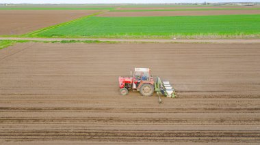 Manzaranın üstünde, ekilebilir tarla, toprak, yeni tahıl, mısır ve mısır eken mekanik tohum makinesini çeken bir traktör var..