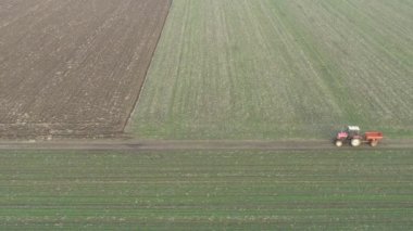 Traktörün görüş alanının üstünde, kırsal kırsal yolda giderek yapay gübre yaymak için monte edilmiş tarım makinesini sürüklüyor..