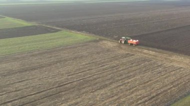 Manzaranın üstünde, çekici, traktörün tepesinde, kimyasal bereketli içi doldurulmuş çuvallarla dolu bir zirai karavanı sürüklüyor, kırsal kırsal yolda giderek yapay gübre yayıyor..
